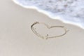 Foamy wave, washing over light sand with outline drawing of heart symbol. Tropical beach.