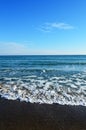 Foamy waves in blue sea with beach. Light blue sky. Royalty Free Stock Photo