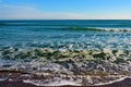 Foamy waves in blue sea with beach. Light blue sky. Royalty Free Stock Photo