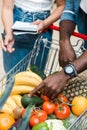 Focus of african american man pointing with finger at shopping cart with groceries near woman with notebook