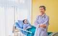 Focus of asian female patient on the bed.  with Old Doctor Standing in room hospital. Royalty Free Stock Photo