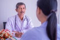 Focus of Asian mature male doctor and female patient sitting talking in hospital. Royalty Free Stock Photo