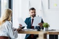 Focus of bearded recruiter holding papers near blonde employee