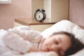 Focus on black alarm clock showing half past six, on bedside nightstand, in blurred foreground of a sleeping child girl Royalty Free Stock Photo