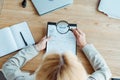 Focus of blonde woman holding magnifier near clipboard