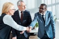 Focus of businessman in glasses looking at handsome african american man shaking hands with blonde woman in office Royalty Free Stock Photo