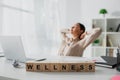 Focus of businesswoman relaxing at workplace with laptop and alphabet cubes with wellness word