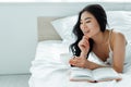 Focus of cheerful brunette asian woman lying near book and holding cup of tea Royalty Free Stock Photo