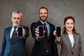 Focus of cheerful businessmen and businesswoman holding smartphones with blank screens on grey