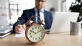 Focus on clock with busy young businessman on background. Royalty Free Stock Photo