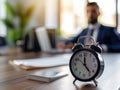 Focus on clock on table with busy young businessman in formal wear, time management concept Royalty Free Stock Photo