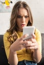 Focus of confused woman holding smartphone while sitting on couch Royalty Free Stock Photo