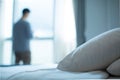 Young businessman standing at hotel window looking out. Bed made up with white pillows and bed sheets in cozy room.