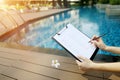 Focus on document, girl fills empty paper on background of pool. Front used with Open Font License