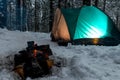 focus on the fire in the snow against the background of the green tent in the winter forest