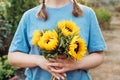 Focus on fresh sunflowers bouquet in hands of young female farmer on the green trees background. Growing flowers. Rural