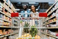 Focus of fruits in shopping cart near happy interracial couple in store