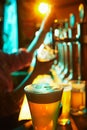 Focus on glass with foamy lager beer and blurred image of bartender pouring another glass of beer in pub on background. Royalty Free Stock Photo