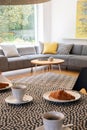 Focus on a gray corner sofa by a big window and a round table and blurry foreground with pastries and coffee in a modern coffee sh