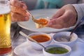 Focus on the hands of a Caucasian woman enjoying the food at the restaurant table tasting the three typical sauces of the Canary