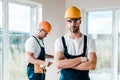 Focus of handsome handyman in goggles standing with crossed arms near coworker Royalty Free Stock Photo