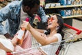 Focus of happy asian girl sunglasses and holding bottle with wine while sitting in shopping cart and looking at cheerful Royalty Free Stock Photo