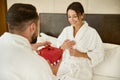 Focus on a happy stunning brunette woman, beloved wife overjoyed to receive a red gift box from her loving partner, husband, Royalty Free Stock Photo