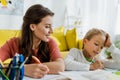 Focus of happy babysitter looking at kid studying in living room