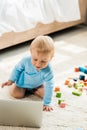 Focus of happy toddler kid looking at laptop near colorful toy blocks on carpet Royalty Free Stock Photo