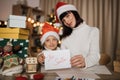 Focus on letter Santa, blured young beautiful mother and little cute child daughter in red hats Royalty Free Stock Photo