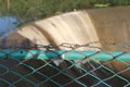 Focus on metal mesh fencing around the local dam, behind which you can see the overflow dam Royalty Free Stock Photo