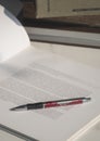 Red pen on white book page with part of textbooks stack on white table in library Royalty Free Stock Photo