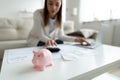 Focus on piggybank with blurred woman calculating budget on background.
