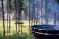 Focus on a portable charcoal grill at a campsite overlooking a green forest