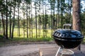 Focus on a portable charcoal grill at a campsite overlooking a green forest