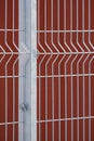 Prefabricated fence post and grating wire panels with blurred red steel wall background