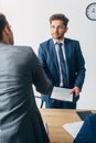 Focus of recruiter with clipboard shaking hands with employee in office