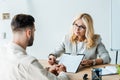 Focus of recruiter in glasses holding pen near clipboard and looking at bearded man