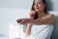 Focus on the remote controller. Pretty young woman sitting on the bed at morning time in her room Royalty Free Stock Photo