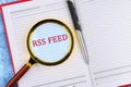 Focus on RSS Feed Highlighted in a Notebook With a Magnifying Glass and Pen Placed Beside It on a Textured Surface Royalty Free Stock Photo