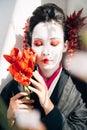 Focus of sakura branches and beautiful geisha holding red flowers with closed eyes in sunlight