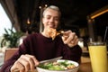 Focus on slice of chicken with cheese. Healthy food concept. Blurred blond man eating caesar salad and drinking orange Royalty Free Stock Photo