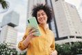 Focus on smartphone. Young hispanic woman typing on cellphone and smiling outdoors. Unfocused happy person using a Royalty Free Stock Photo