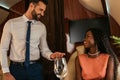 Focus of smiling air steward looking at happy, elegant african american woman in private plane