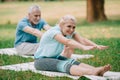 Focus of smiling, mature man and woman sitting in stretching poses while practicing yoga in park Royalty Free Stock Photo