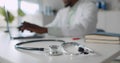 Focus on stethoscope lying on table and African-American doctor typing on laptop over blurred background