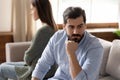 Focus on stressed young man sitting separate from offended wife.