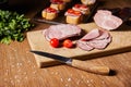 Focus of tasty ham slices, cherry tomatoes and knife on cutting board near parsley and canape