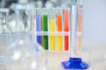 Focus on test tubes with rainbow colored chemicals standing on tripod. Blurred foreground with graduated glass labware