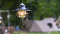 Vintage black camping lantern with blurred background of tents in camping area at natural parkland